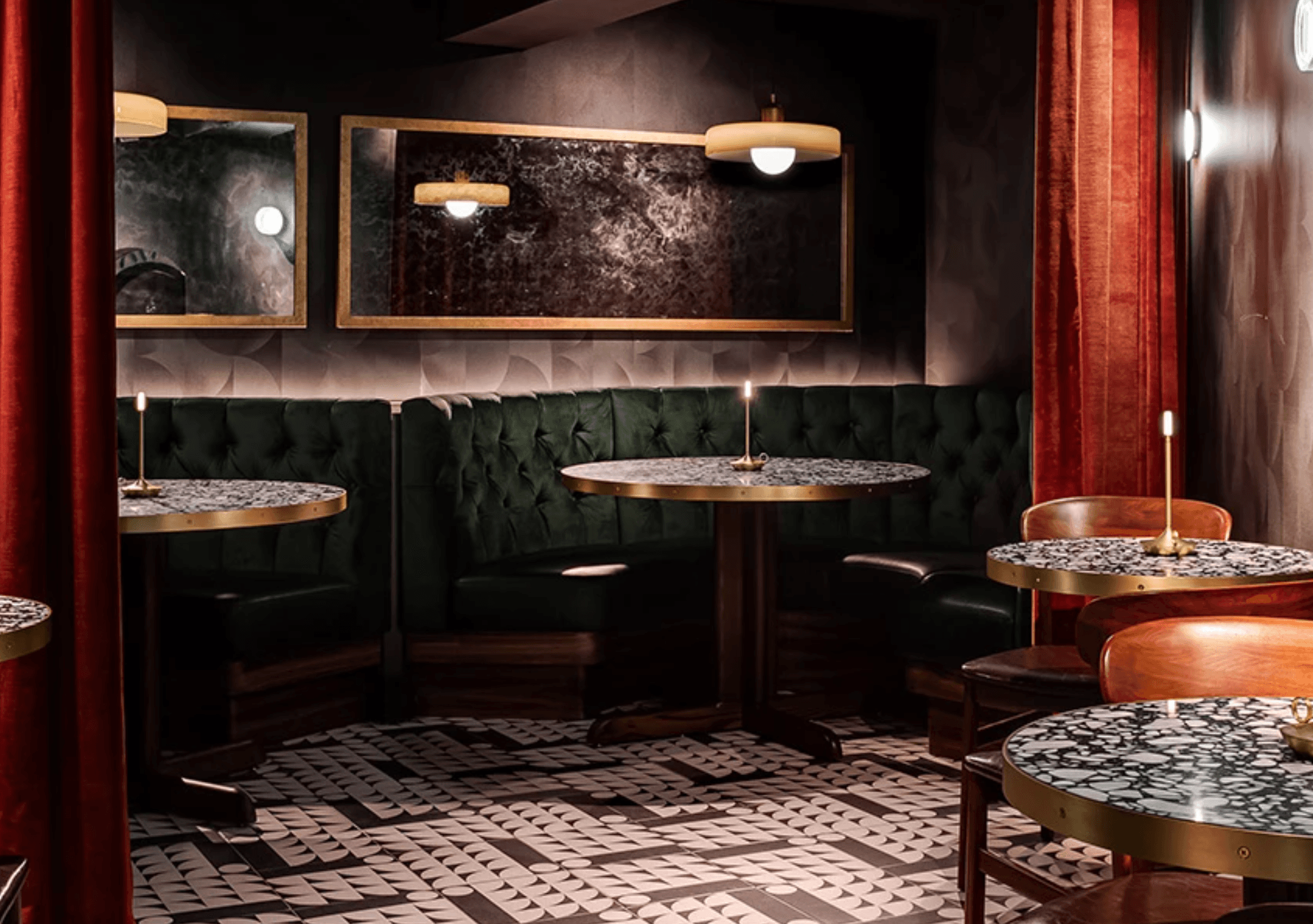 Dining area with circular dark marble tables, high-backed dark green velvet circular booths, tiled floors, and moody lighting.and marb