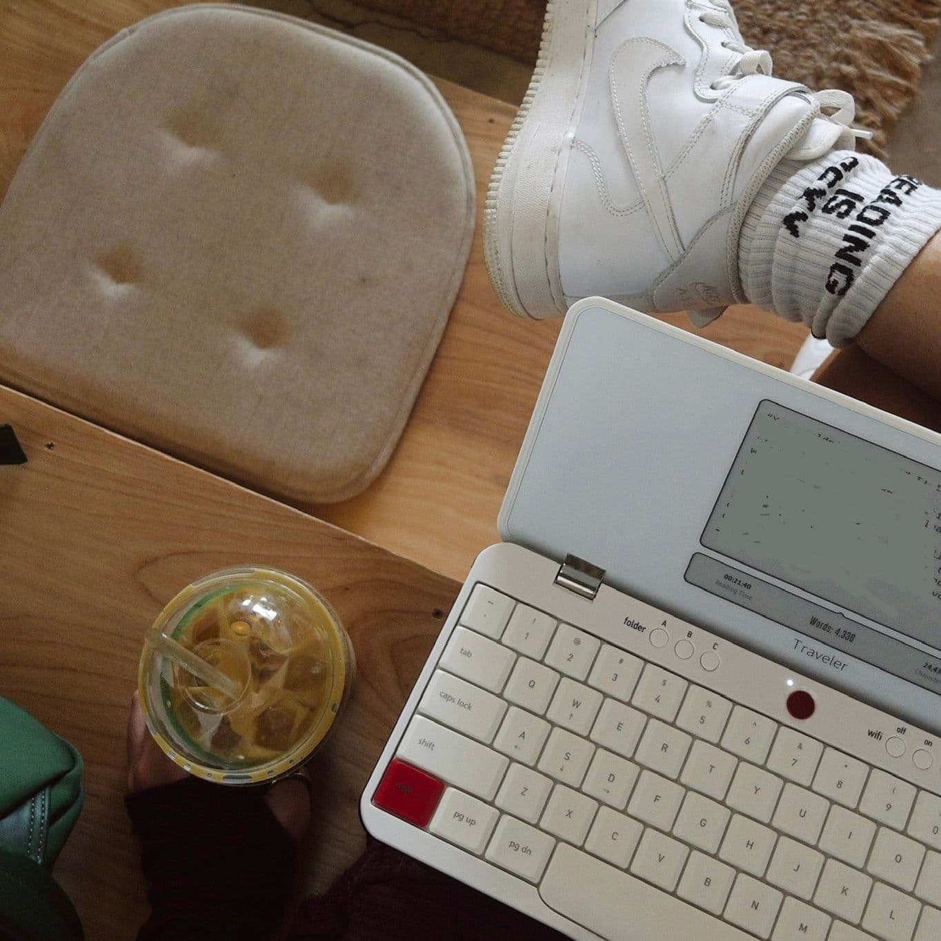Freewrite gadget open on lap with an iced coffee beside on the table.