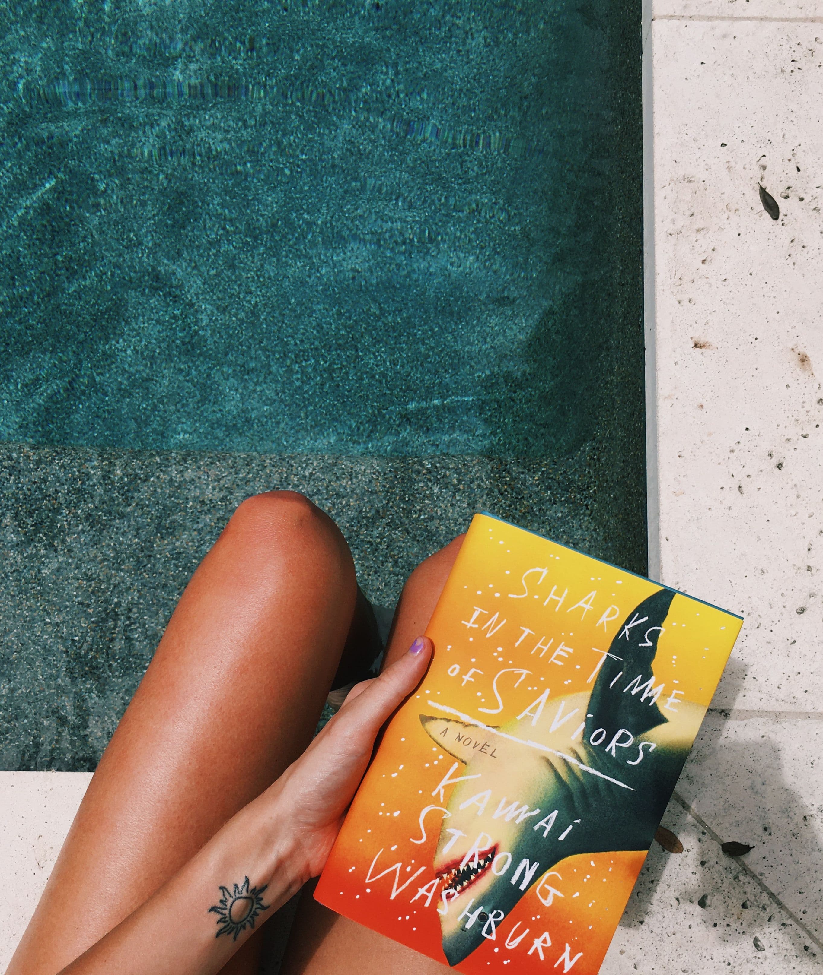 sharks in the times of saviors book held on the edge of a pool