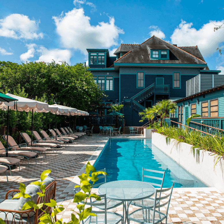 intimate pool and a line of pink vintage-style chaise loungers with umbrellas, with dark blue boutique hotel mansion in background