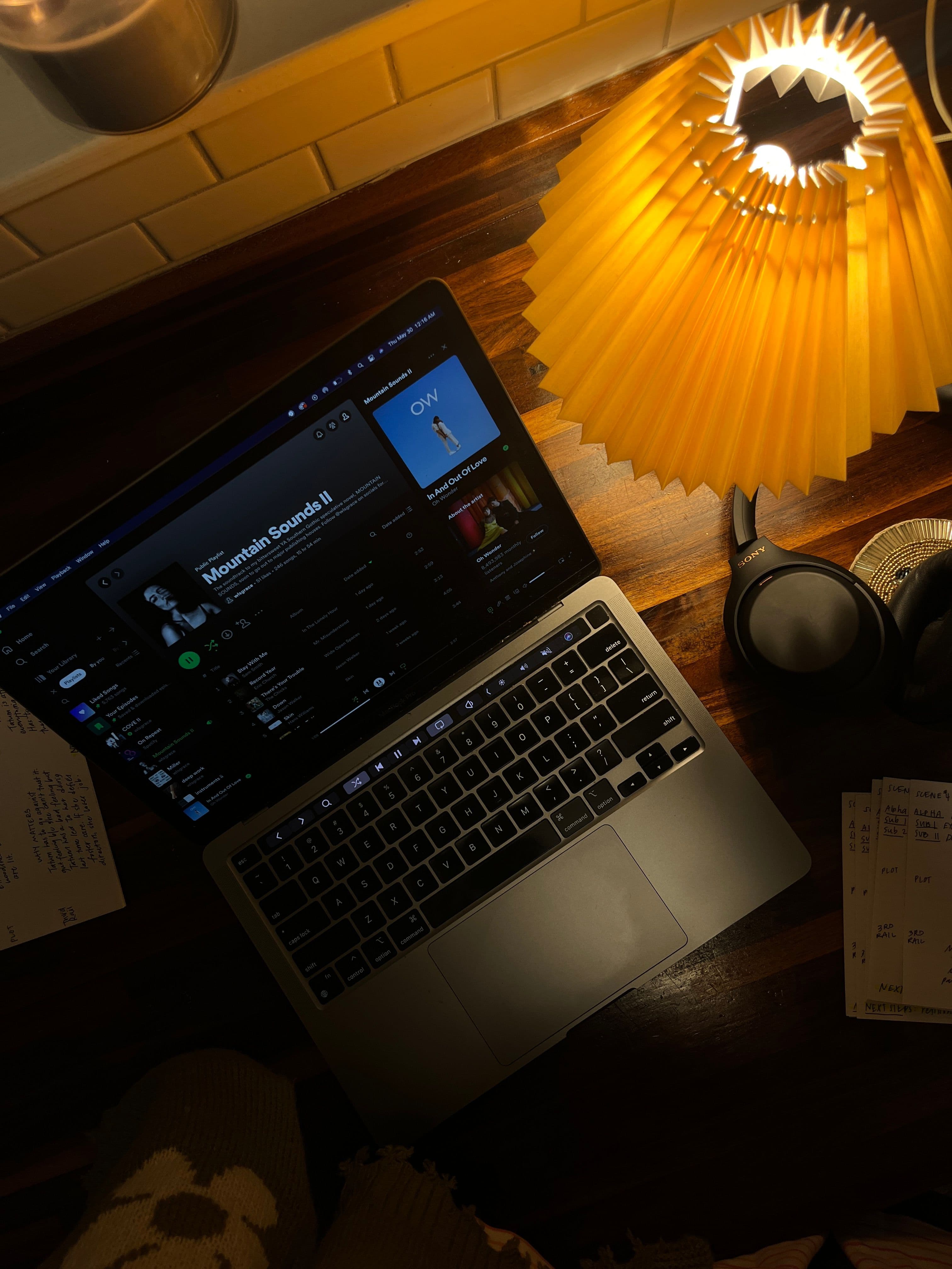 Computer open to a playlist in a dark room shot from overhead with an amber lamp beside