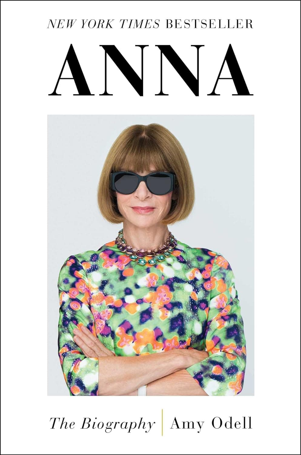 Fashionable woman in multicolored top and stylish bob with sunglasses, arms crossed.